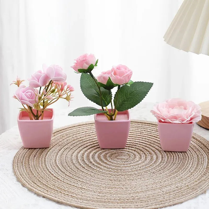 A set of three pink artificial rose potted plants displayed on a woven mat.