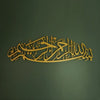 Gold metal calligraphy of Bismillah written in Arabic script on a dark green wall.