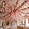 A chandelier adorned with pink silk wisteria hanging vine garlands above a formal dining room.