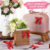 Pink satin bow boxes and red ribbon bows displayed on a wooden surface.