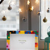 A colorful DIY photo frame made of decorative blocks displayed in front of a window with string lights.