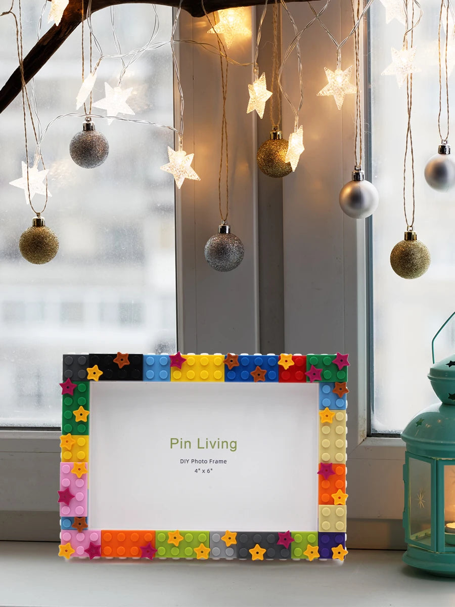 A colorful DIY photo frame made of decorative blocks displayed in front of a window with string lights.