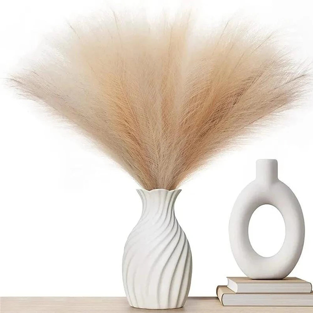 A bouquet of dried beige pampas grass arranged in a white vase on a wooden surface.