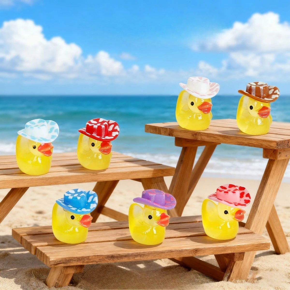 A collection of glow-in-the-dark resin duck figurines with colorful hats sitting on wooden planks on a sandy beach.