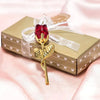 Goldfarbene künstliche Rose mit rotem Kristallzentrum, mit durchsichtiger Schleife auf einer hellgrünen Geschenkbox
