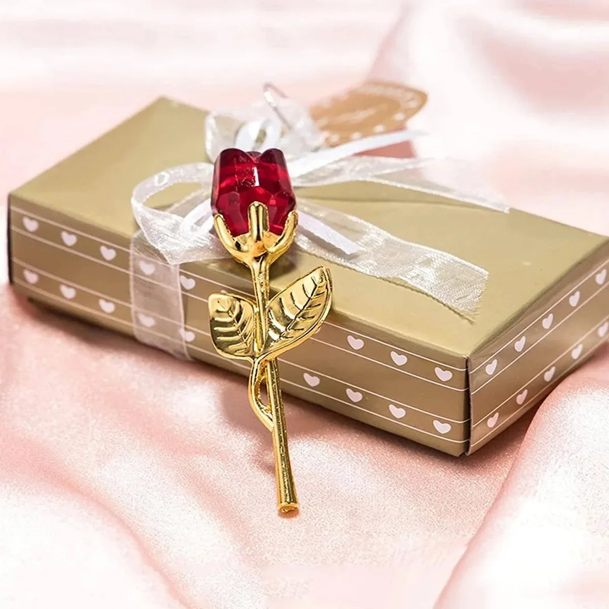 Goldfarbene künstliche Rose mit rotem Kristallzentrum, mit durchsichtiger Schleife auf einer hellgrünen Geschenkbox