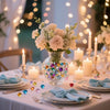 A floral centerpiece with light pink and white flowers sits on a table set for an event, featuring blue ribbon accents.