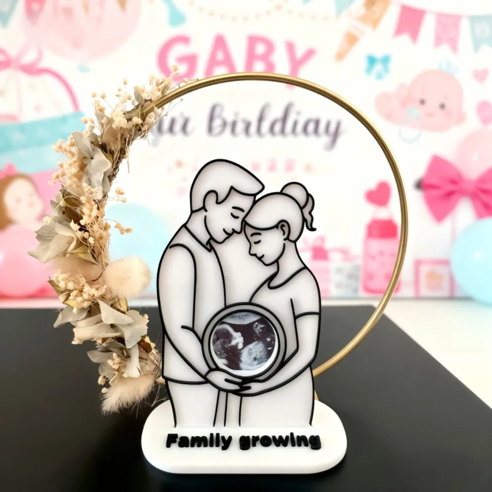 A white silhouette of a mother and baby embracing, framed by a gold hoop and decorated with dried flowers.