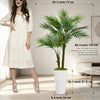 A tall artificial areca palm tree in a white pot displayed next to a woman wearing a white dress.