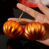 Two shiny metallic orange pumpkin hanging ornaments held in a hand.