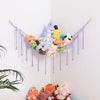 A purple fabric hammock displaying various cute stuffed animals and plushies hanging on a white wall.