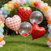 A display of colorful balloons forming an archway with a large strawberry balloon centerpiece and heart-shaped balloons.