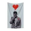 A portrait of a man with his hand to his face, set against a light gray flag tapestry featuring a red heart.