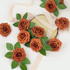 A cluster of artificial real touch foam roses in various shades of burnt orange and brown with green leaves and natural twine