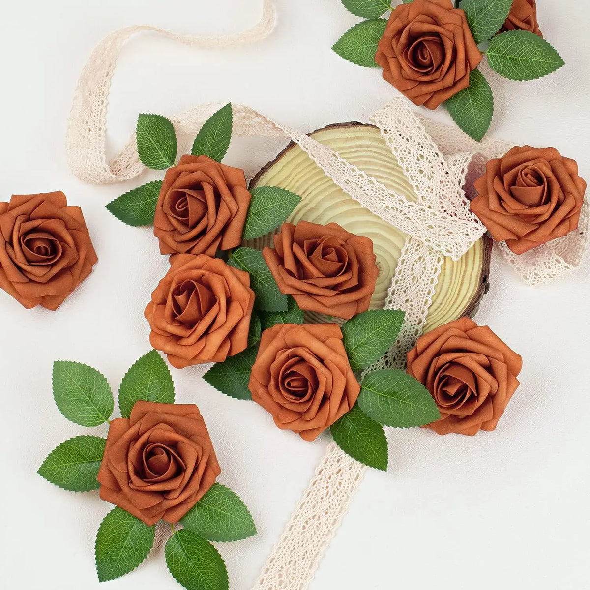 A cluster of artificial real touch foam roses in various shades of burnt orange and brown with green leaves and natural twine