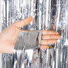 A hand is holding silver metallic foil fringe curtain fabric, showing the shiny texture and vertical strands.