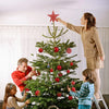 A family is decorating a Christmas tree with ornaments and a star topper in a bright room.