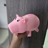 A hand holds a pink piggy bank with a cartoon face against a gray wooden surface.