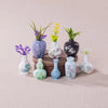 A set of eight mini resin vases with various floral patterns and colors displayed on a light pink surface.