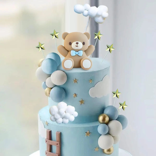 A two-tiered light blue cake decorated with clouds, stars, and a teddy bear topper.