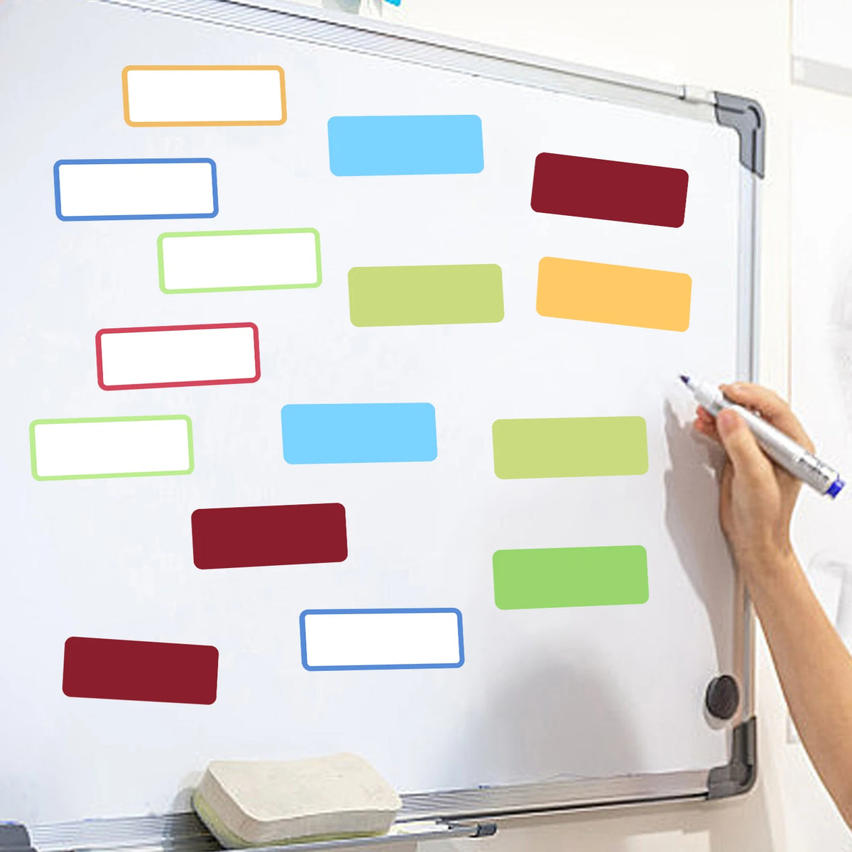 A hand writes on a whiteboard covered with colorful rectangular labels and stickers.