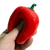 A hand is holding a bright red, squishy bell pepper stress relief block with a green stem.