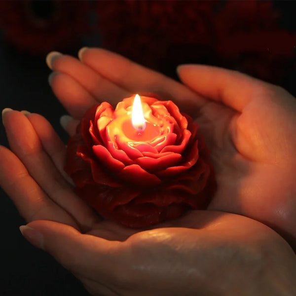 A hand gently holds a handcrafted rose-shaped scented candle glowing brightly.