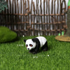 A realistic black and white panda figurine is placed on green grass with measurement lines.