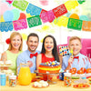 A colorful fiesta papel picado bunting banner decorated with bright paper flags and fruit on a table.