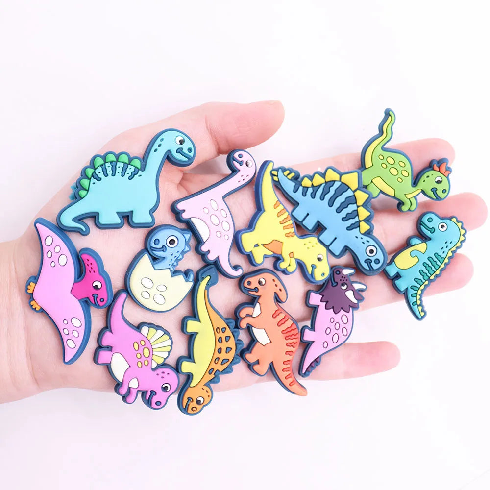 A hand holds a set of twelve colorful cartoon dinosaur PVC shoe charms.