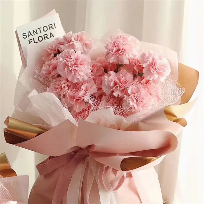A bouquet of pink carnations wrapped in sheer paper with a sign reading SANTORI FLORA