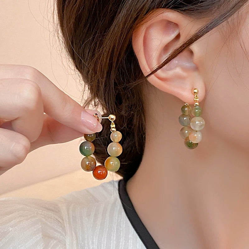 Gold and green resin beaded drop earrings worn by a person's ear.
