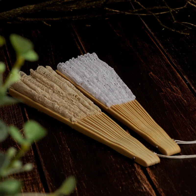A wooden hand fan with a white lace folding fan resting on a dark wooden surface.