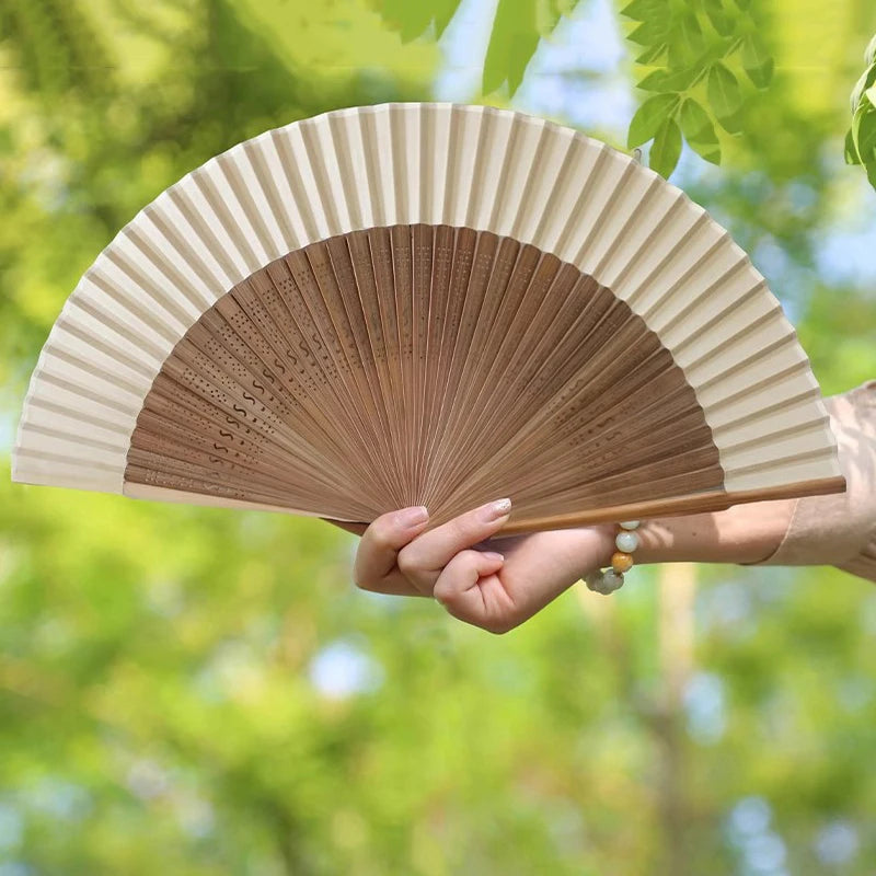 A hand holding an elegant bamboo folding fan with a tassel, showing the pleated fan surface.