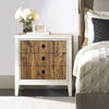 A white dresser with wood grain drawers decorated with white flowers and neutral bedding.
