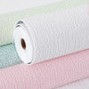 Rolls of self-adhesive 3D linen texture wallpaper panels in white, mint green, and pink.