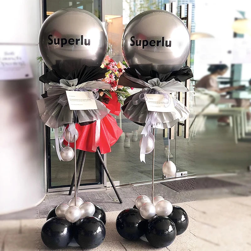 Two silver balloons displayed on an adjustable metal column stand with black and red ribbon accents.