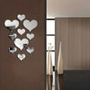 A set of silver heart-shaped mirror wall stickers mounted on a brown wall next to a modern interior with light wood paneling.
