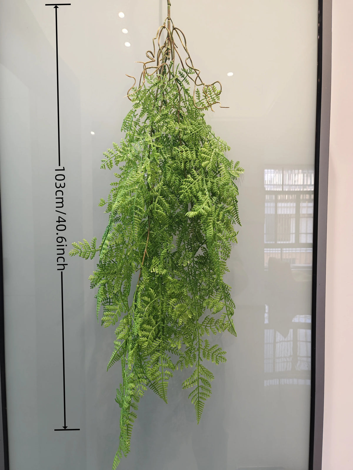 Artificial hanging ivy vine with long green leaves displayed against a glass panel.