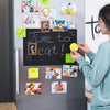 A person is decorating a refrigerator with various photos and Halloween-themed magnets on a gray surface.
