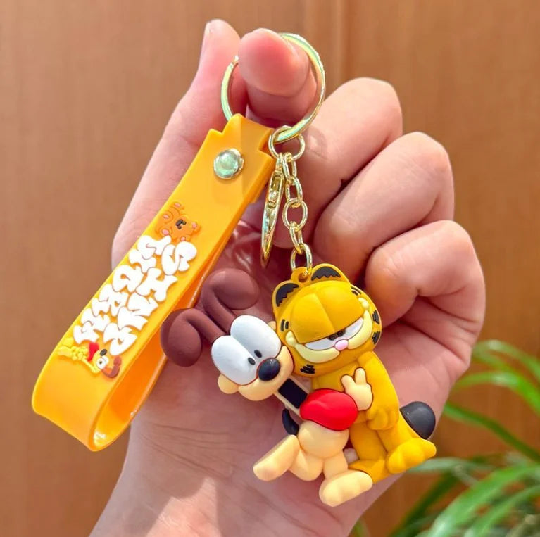 A hand holds a yellow Garfield cartoon keychain pendant with a gold chain and orange tag.