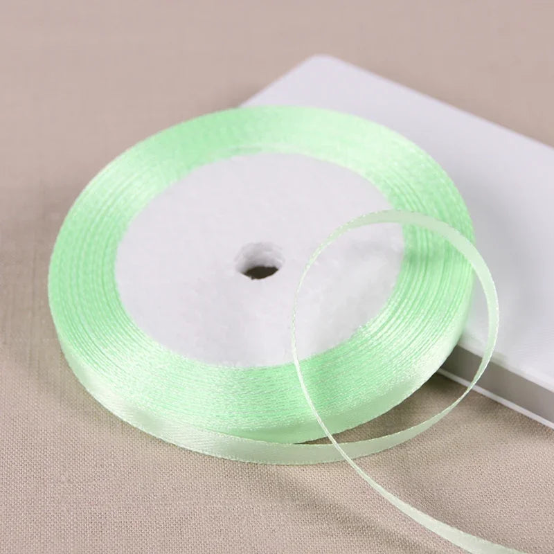 A roll of light green satin ribbon on a white spool, ready for gift wrapping or DIY crafts.