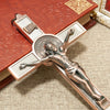 A bronze crucifix wall decor featuring a figure of Christ, St. Benedict medal, and INRI inscription on a wooden book backgrou