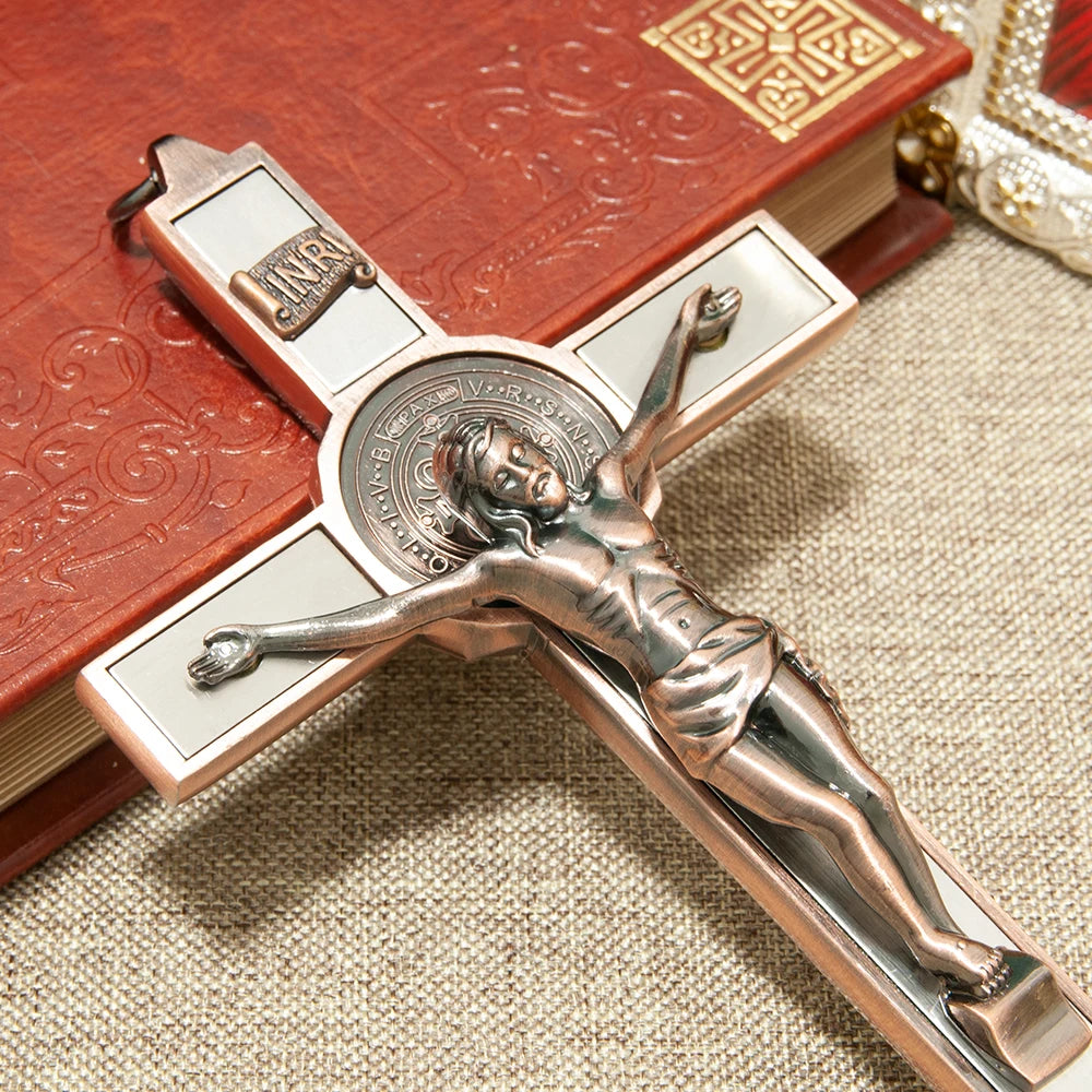 A bronze crucifix wall decor featuring a figure of Christ, St. Benedict medal, and INRI inscription on a wooden book backgrou