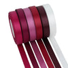 A set of satin silk ribbons in various shades of pink and burgundy rolled together.