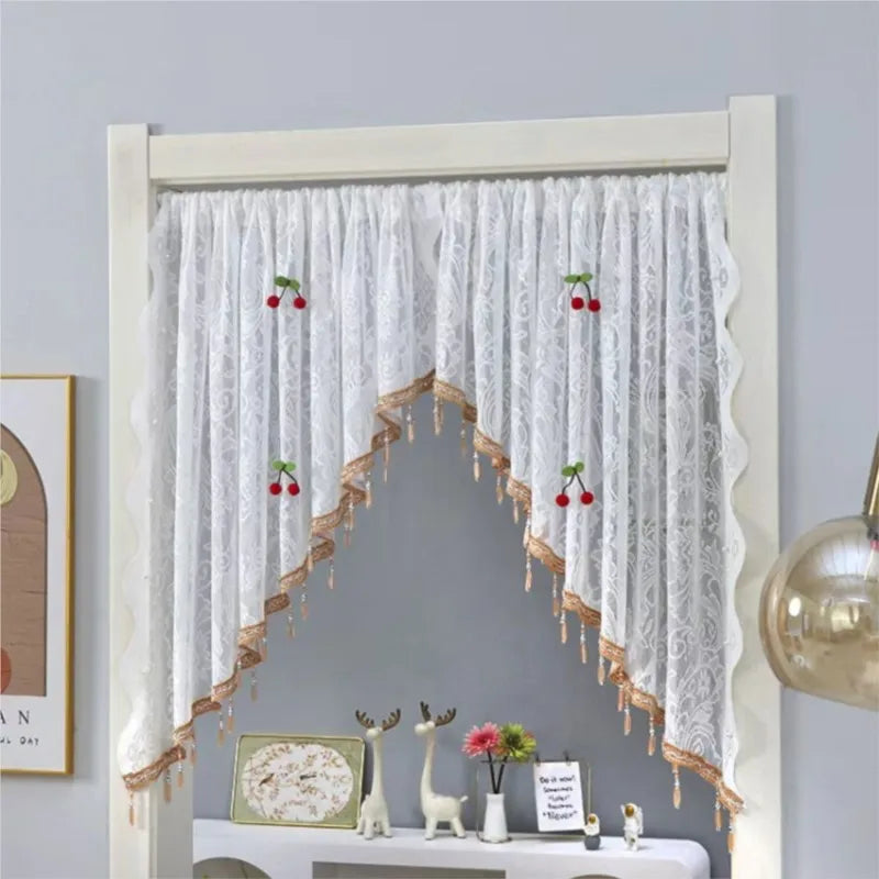 White lace door curtain with red berries and gold fringe draped over a white wooden frame.