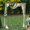 Une arche décorée d'un drapé en tissu crème et de guirlandes d'eucalyptus vert en extérieur.