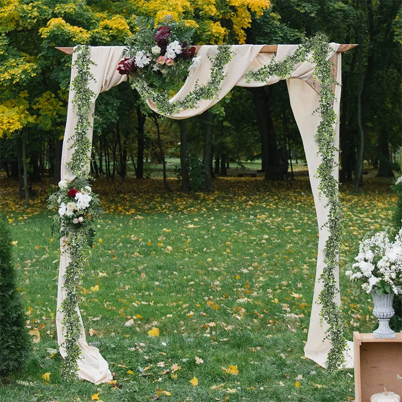 Une arche décorée d'un drapé en tissu crème et de guirlandes d'eucalyptus vert en extérieur.