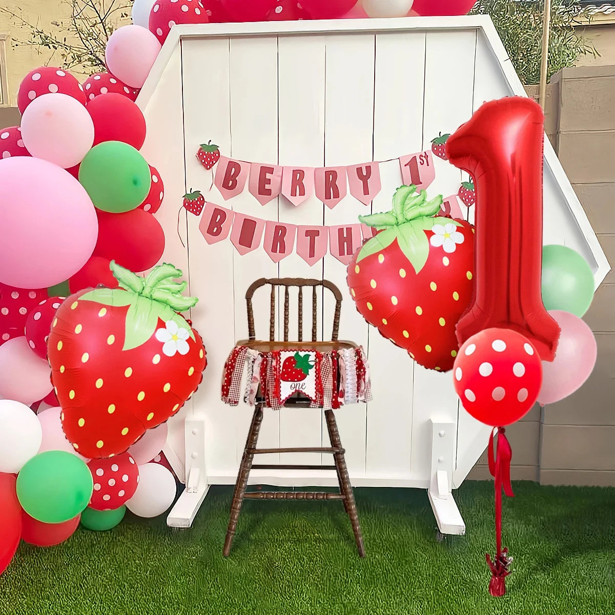 A red and pink strawberry foil balloon decoration with a wooden chair backdrop.