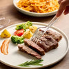 A fork is lifting slices of cooked meat and vegetables from a white plate, with more food visible in the background.